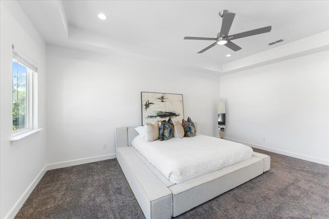 bedroom with dark colored carpet, ceiling fan, and a raised ceiling