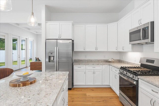 kitchen featuring stainless steel appliances, white cabinetry, light stone countertops, light hardwood / wood-style flooring, and pendant lighting