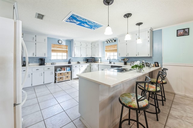 kitchen with white fridge, white cabinetry, a breakfast bar, and kitchen peninsula