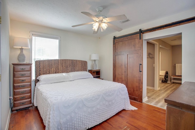 bedroom with a barn door, hardwood / wood-style flooring, and ceiling fan