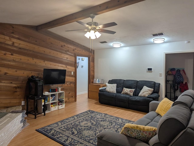 living room featuring beamed ceiling, ceiling fan, wooden walls, and light hardwood / wood-style floors