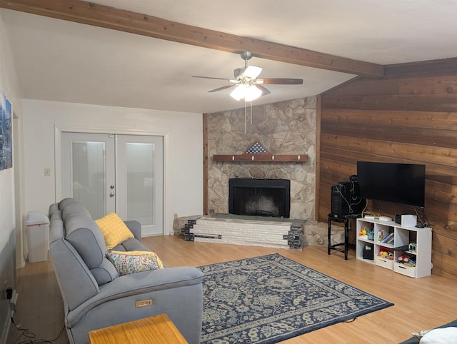 living room with french doors, a stone fireplace, vaulted ceiling with beams, wood-type flooring, and ceiling fan