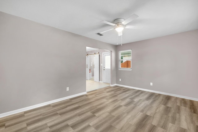 empty room with ceiling fan, a barn door, and light hardwood / wood-style flooring