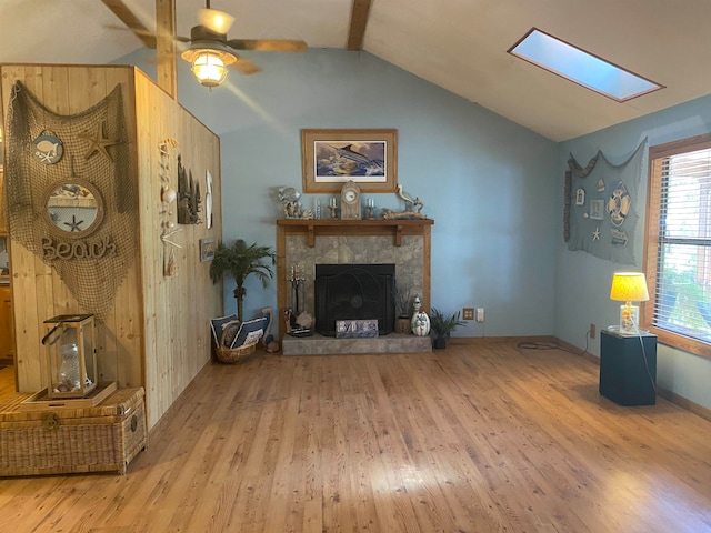 living room with a fireplace, light hardwood / wood-style flooring, ceiling fan, and lofted ceiling with skylight