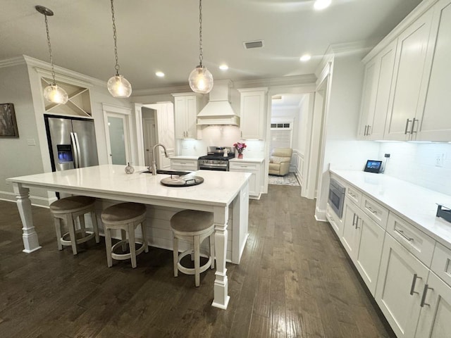 kitchen with a center island with sink, white cabinets, custom exhaust hood, and stainless steel appliances