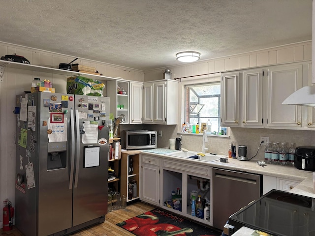 kitchen featuring sink, a textured ceiling, stainless steel appliances, light hardwood / wood-style floors, and white cabinets