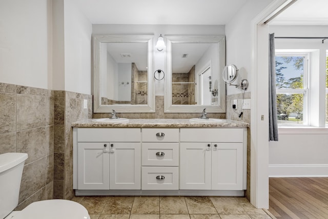 full bath featuring toilet, double vanity, tile walls, and a sink