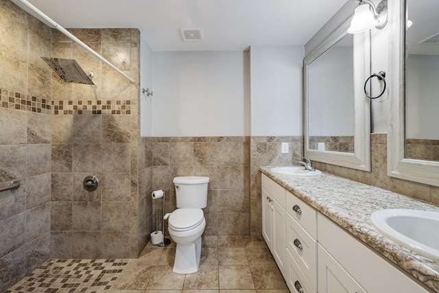 bathroom with toilet, a sink, visible vents, tile walls, and double vanity