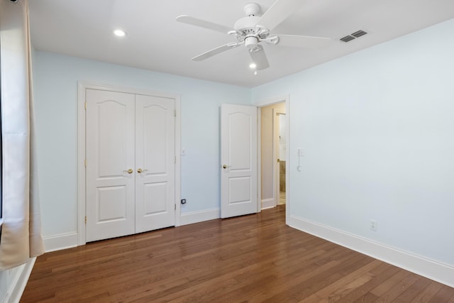 unfurnished bedroom featuring dark wood-style flooring, a closet, visible vents, a ceiling fan, and baseboards