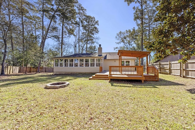 back of house featuring a yard, a sunroom, a fenced backyard, a fire pit, and a wooden deck