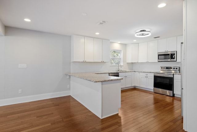 kitchen with visible vents, appliances with stainless steel finishes, white cabinetry, a sink, and a peninsula