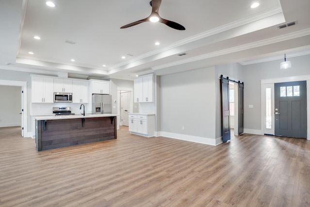 kitchen featuring appliances with stainless steel finishes, white cabinetry, a tray ceiling, a barn door, and a large island with sink