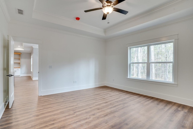 empty room with ceiling fan, crown molding, hardwood / wood-style floors, and a tray ceiling