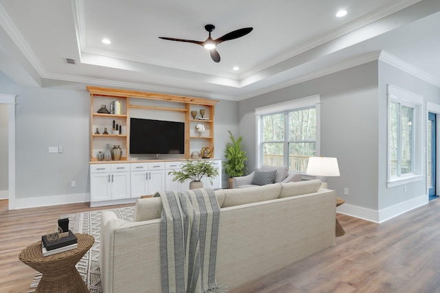 living room with a tray ceiling, ornamental molding, and light wood-type flooring