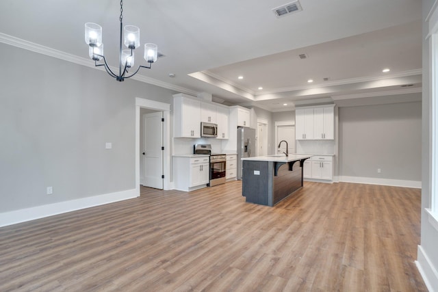 kitchen with white cabinets, appliances with stainless steel finishes, a kitchen island with sink, and an inviting chandelier