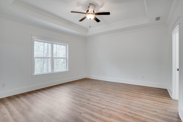 empty room featuring ceiling fan, crown molding, light hardwood / wood-style floors, and a tray ceiling