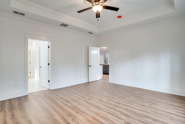 spare room featuring light hardwood / wood-style floors, ornamental molding, a raised ceiling, and ceiling fan