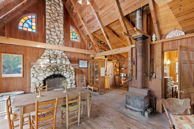 interior space with a stone fireplace, wood-type flooring, a wood stove, wooden walls, and high vaulted ceiling