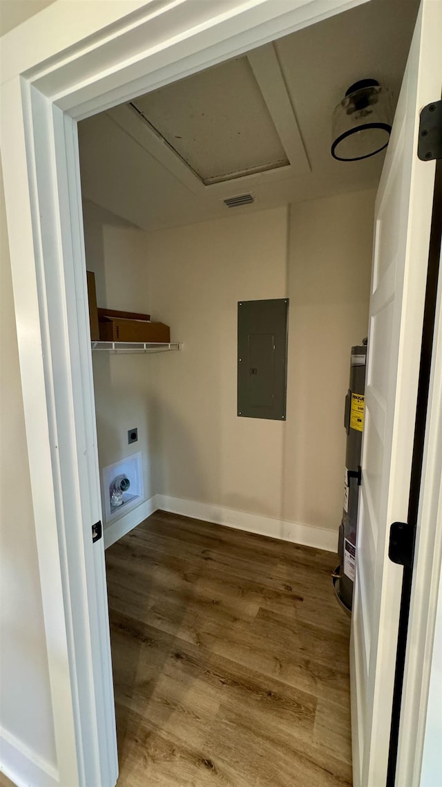 laundry room featuring electric panel, strapped water heater, wood finished floors, and attic access