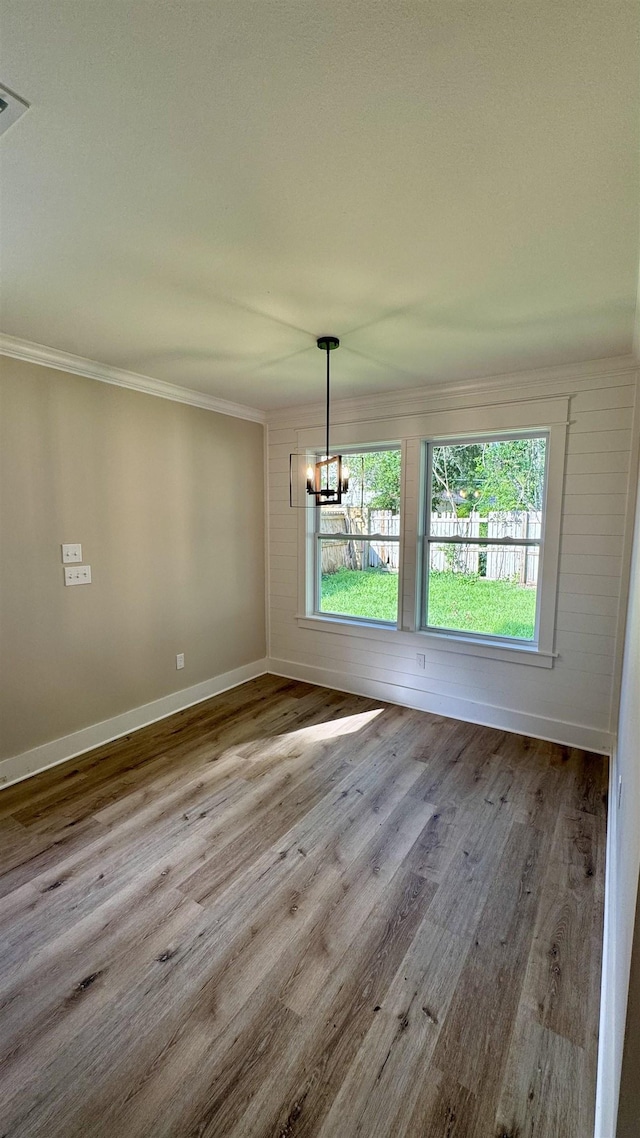 unfurnished dining area with ornamental molding, a chandelier, and wood finished floors