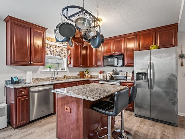 kitchen with a kitchen island, appliances with stainless steel finishes, sink, light stone countertops, and light wood-type flooring