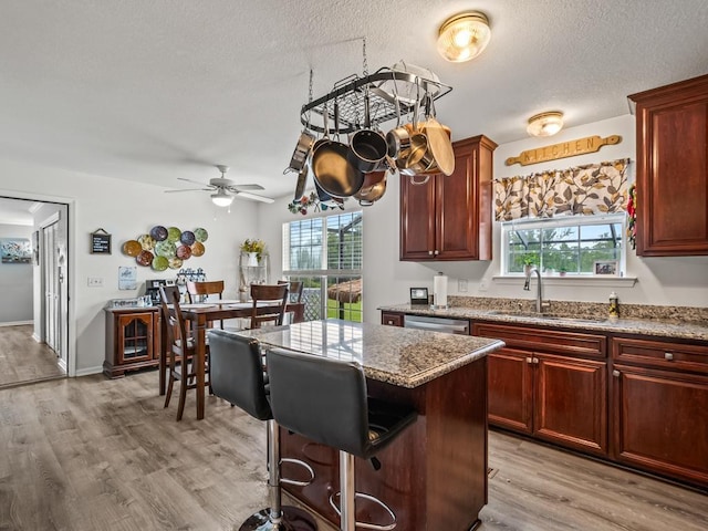 kitchen with sink, light stone counters, a textured ceiling, light wood-type flooring, and a kitchen island