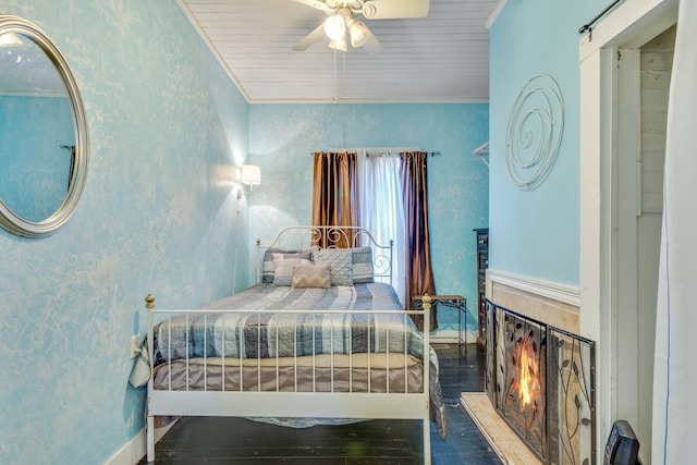 bedroom featuring a barn door, dark wood finished floors, crown molding, and a glass covered fireplace