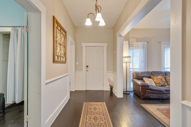 foyer with a wainscoted wall, dark wood-style flooring, and a notable chandelier