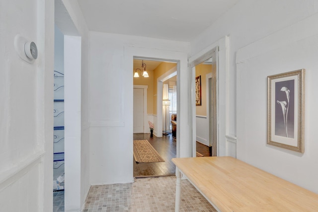 hallway with a wainscoted wall, a chandelier, and wood finished floors