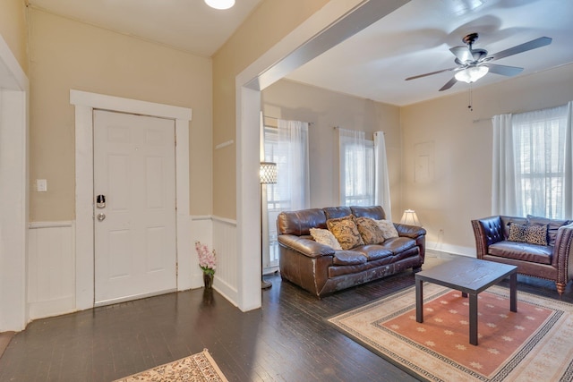 living room with dark wood-style floors, ceiling fan, and a wainscoted wall