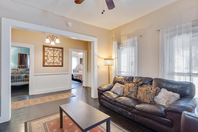 living area featuring ceiling fan with notable chandelier, dark wood-style flooring, and wainscoting