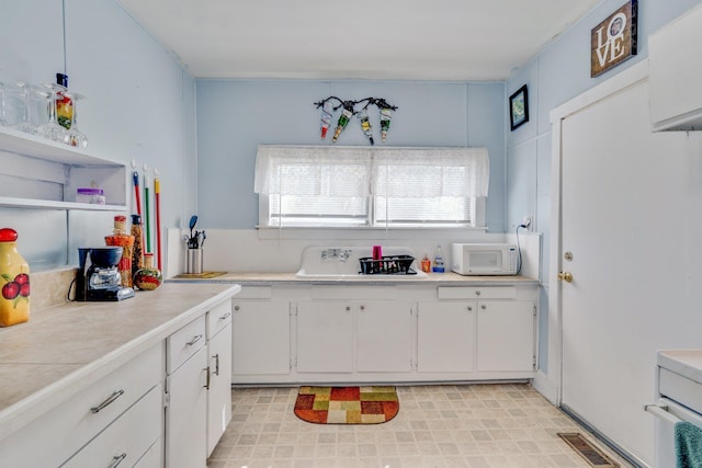 kitchen featuring white microwave, light floors, visible vents, white cabinets, and open shelves