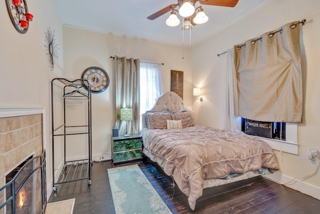 bedroom featuring dark wood finished floors, a tiled fireplace, ornamental molding, cooling unit, and baseboards