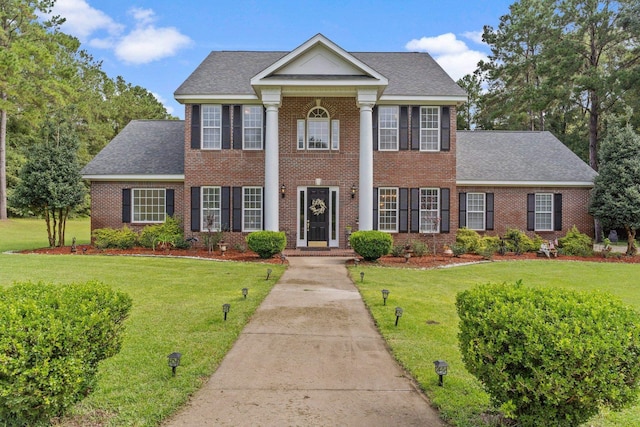 neoclassical / greek revival house featuring a shingled roof, brick siding, and a front lawn