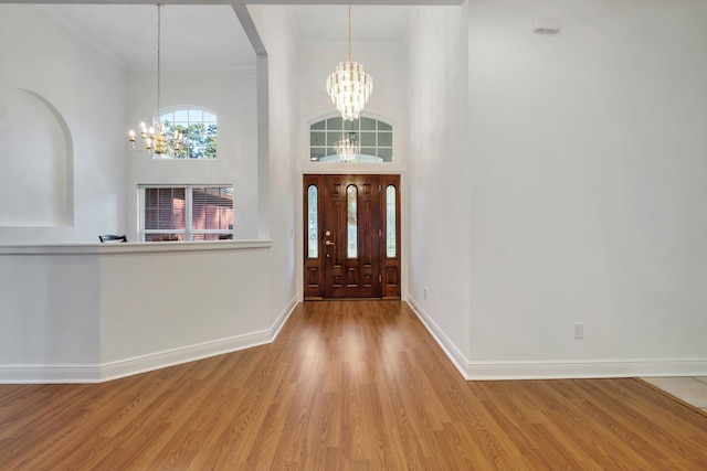 entrance foyer featuring a towering ceiling, hardwood / wood-style floors, a notable chandelier, and ornamental molding