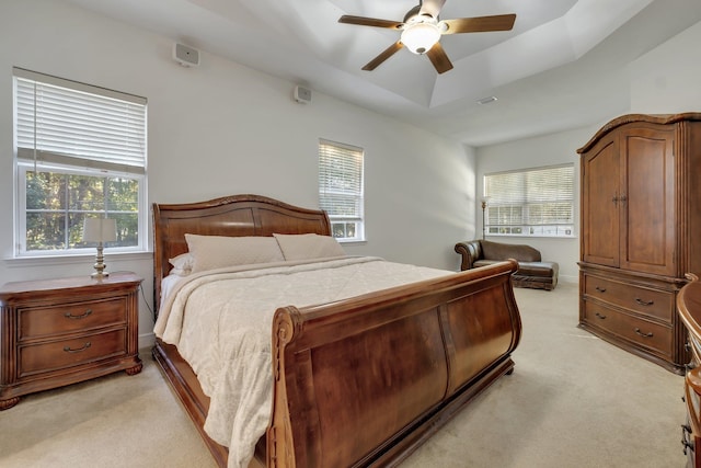 bedroom featuring ceiling fan, light carpet, and a tray ceiling