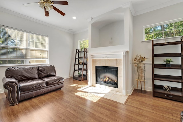 living room with ceiling fan, crown molding, light hardwood / wood-style flooring, and a tiled fireplace