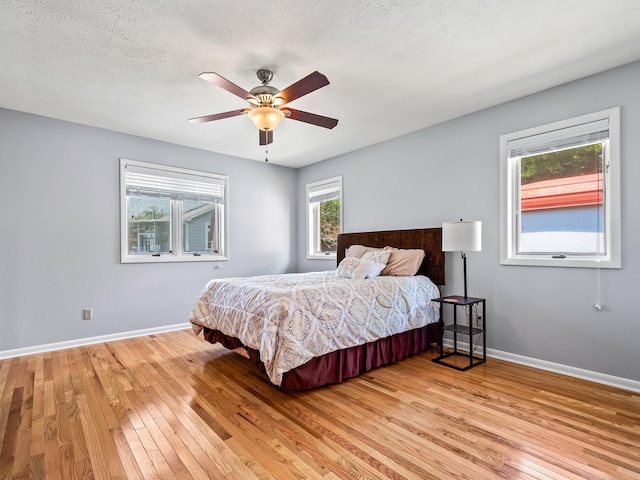 bedroom featuring multiple windows, ceiling fan, light hardwood / wood-style floors, and a textured ceiling