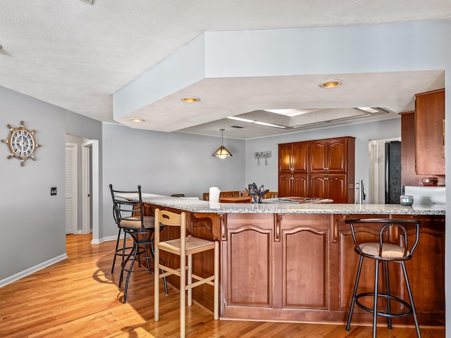 kitchen with pendant lighting, kitchen peninsula, a breakfast bar area, and light hardwood / wood-style flooring