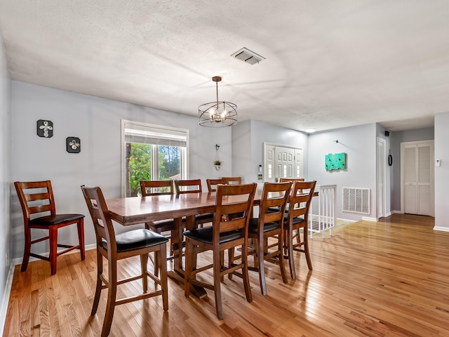 dining area featuring light hardwood / wood-style flooring, a textured ceiling, and a notable chandelier