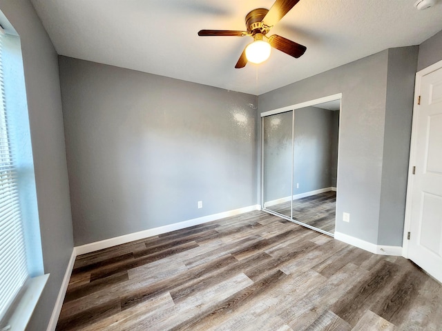 unfurnished bedroom featuring multiple windows, hardwood / wood-style floors, ceiling fan, and a closet