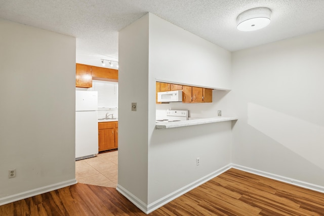 kitchen featuring white appliances, sink, light hardwood / wood-style flooring, a textured ceiling, and kitchen peninsula