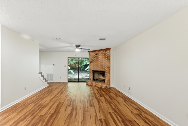 unfurnished living room with ceiling fan, light hardwood / wood-style flooring, a textured ceiling, and a brick fireplace