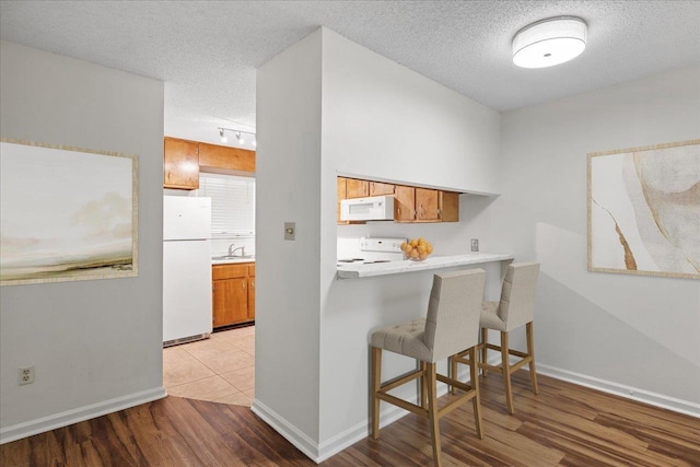 kitchen featuring sink, light hardwood / wood-style flooring, a textured ceiling, white appliances, and a breakfast bar area