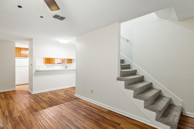 staircase featuring hardwood / wood-style floors, a textured ceiling, and ceiling fan