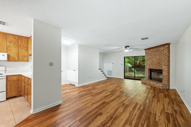 unfurnished living room featuring ceiling fan, light wood-type flooring, a textured ceiling, and a brick fireplace