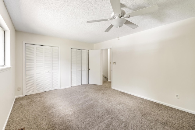 unfurnished bedroom featuring multiple closets, ceiling fan, carpet, and a textured ceiling