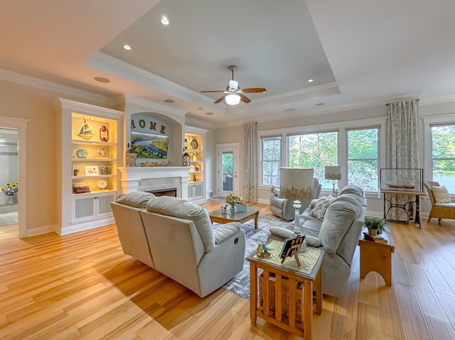 living room with a raised ceiling, light wood-type flooring, ceiling fan, and a fireplace