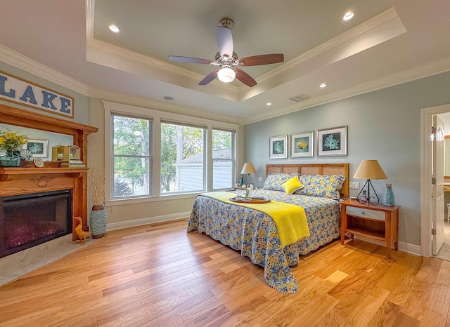 bedroom with crown molding, a fireplace with flush hearth, visible vents, a raised ceiling, and wood finished floors