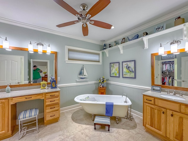 full bathroom featuring vanity, ornamental molding, wainscoting, ceiling fan, and a freestanding bath